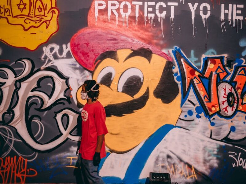 a man in a face mask standing beside a wall with graffiti