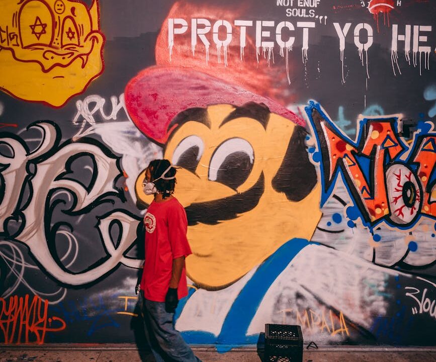 a man in a face mask standing beside a wall with graffiti